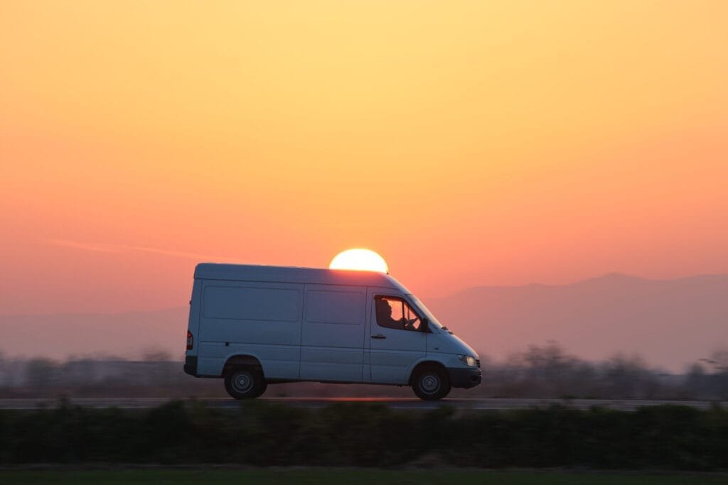 Hvid varevogn kører ved solnedgang.