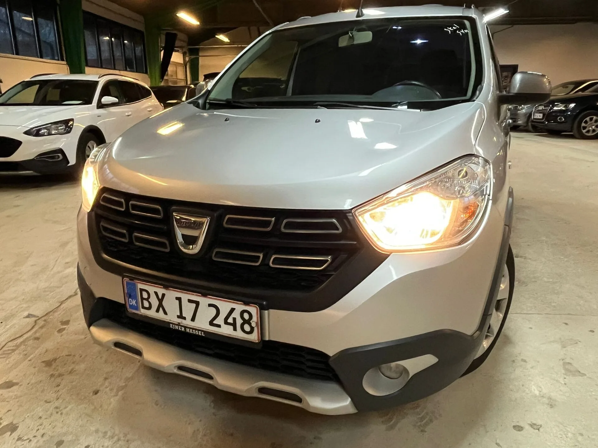 Sølv Dacia bil parkeret indendørs med tændte forlygter