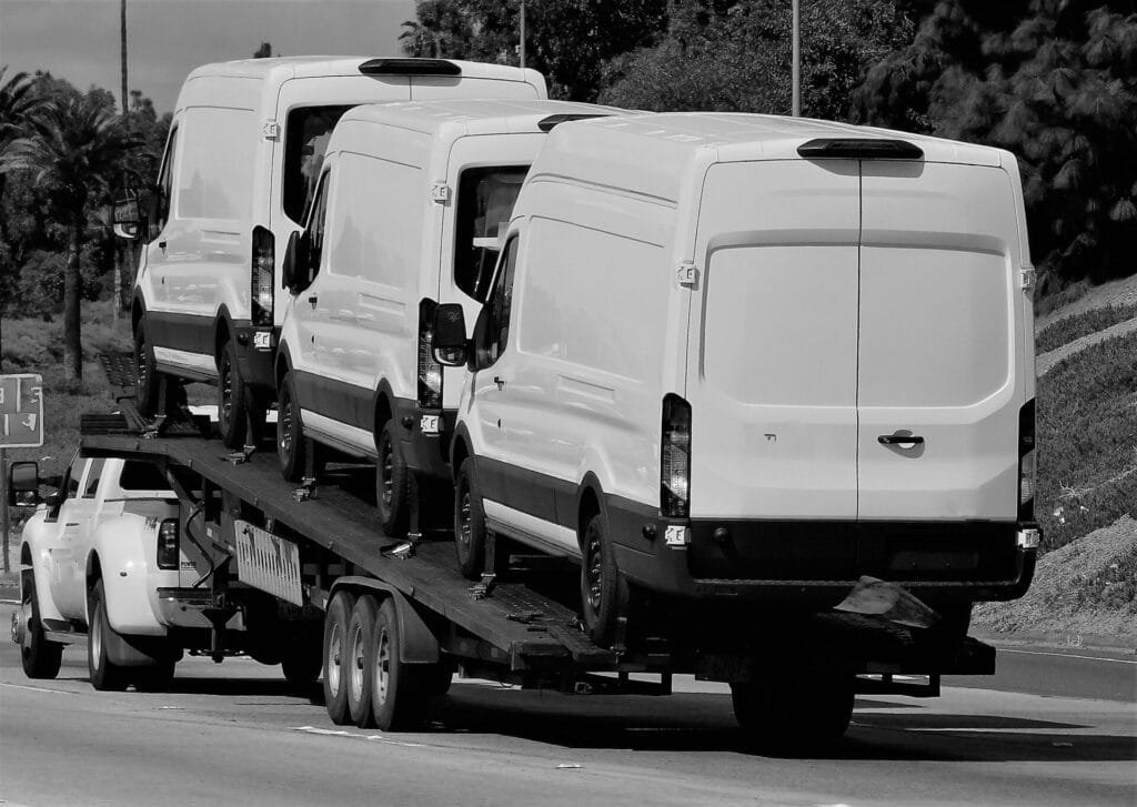 Lastbil transporterer tre hvide varevogne på vej