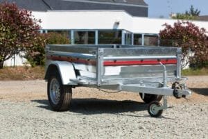 Metallisk trailer parkeret på grus foran hus